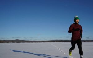 Man running on a snowy field in winter under clear blue skies.