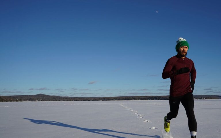 Man running on a snowy field in winter under clear blue skies.