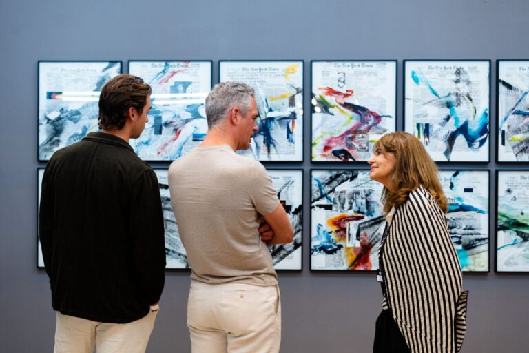 Tres personas conversando frente a obras de arte en una galería