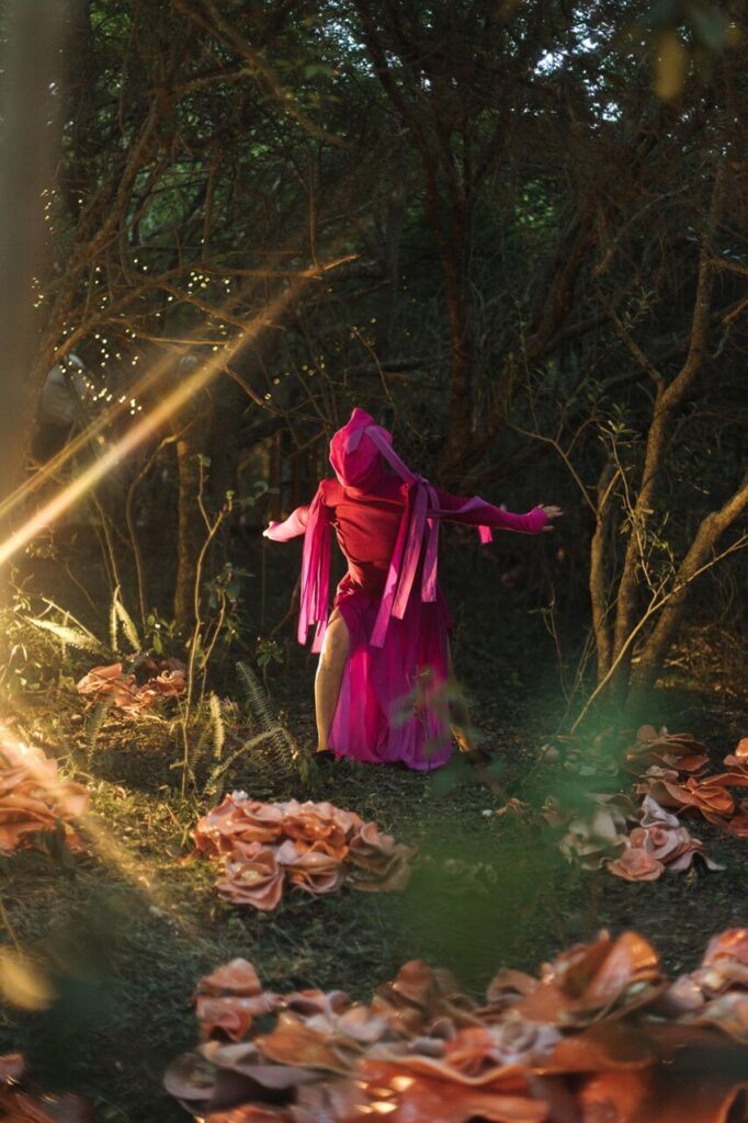 Artista en vestido rosa en un bosque con flores de tela