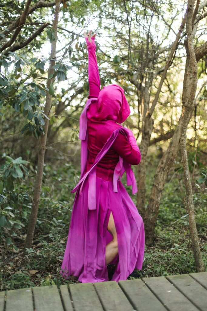 Mujer con vestido rosa en un entorno natural, levantando el brazo.