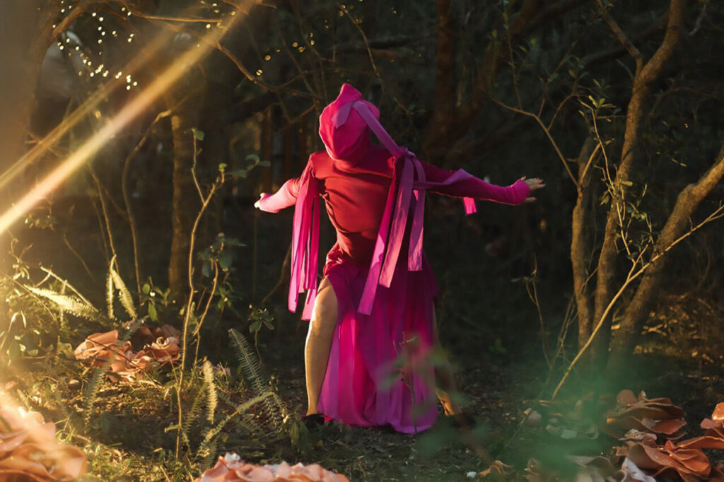 Artista en vestido rosa actuando en un bosque iluminado