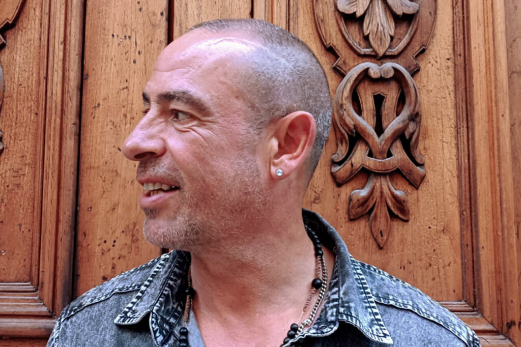 José de Divina sonriendo frente a un fondo de madera tallada