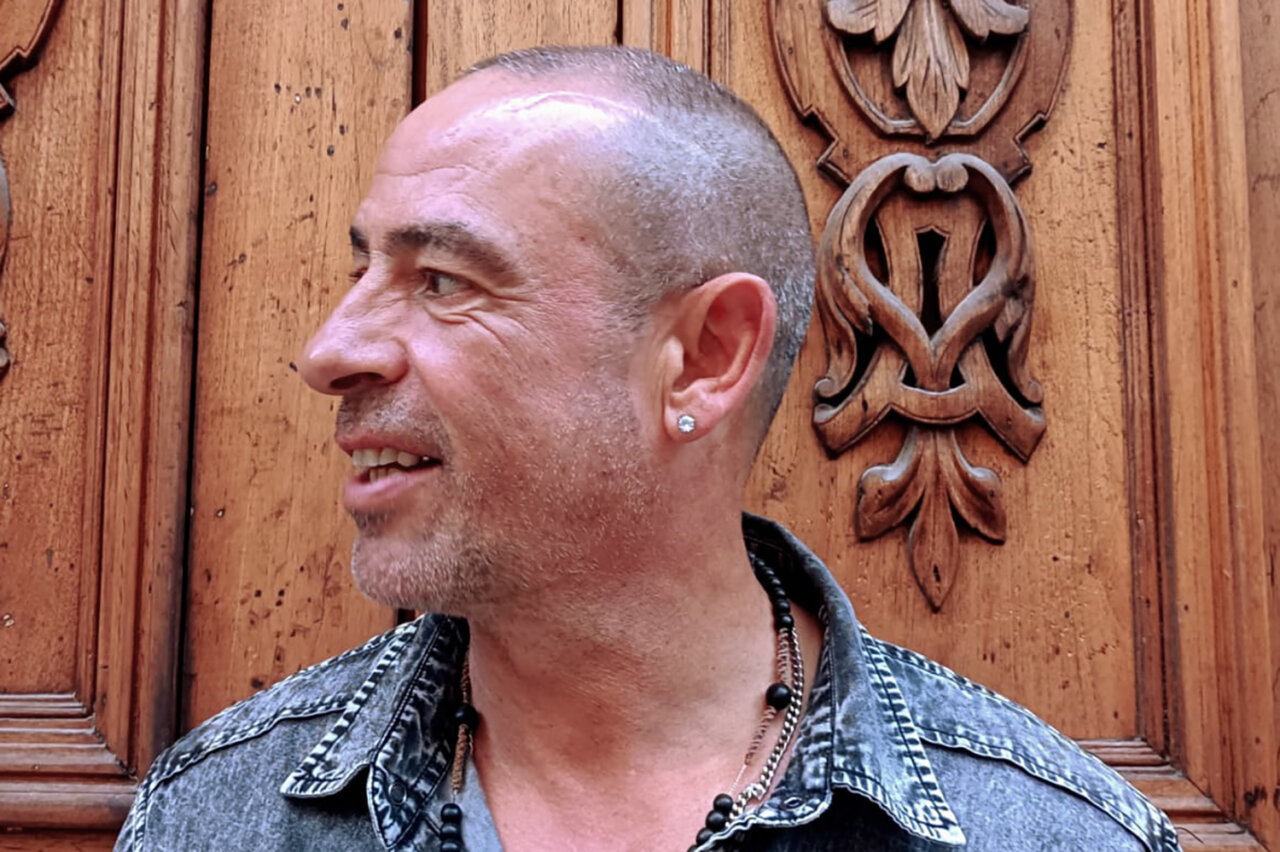 José de Divina sonriendo frente a un fondo de madera tallada