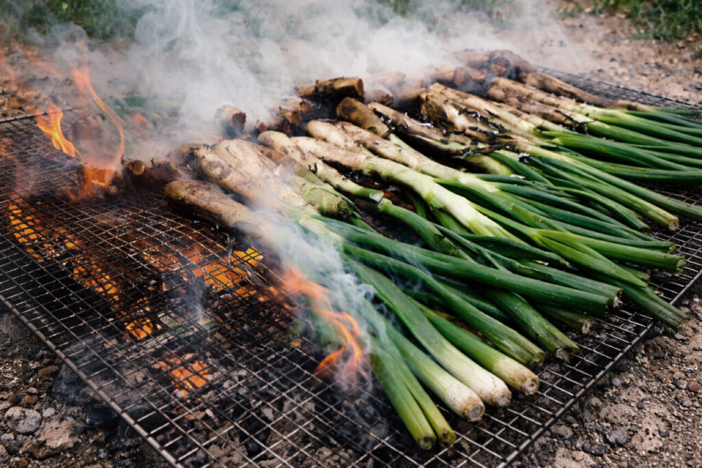 Calçots asándose en una parrilla con humo y llamas.