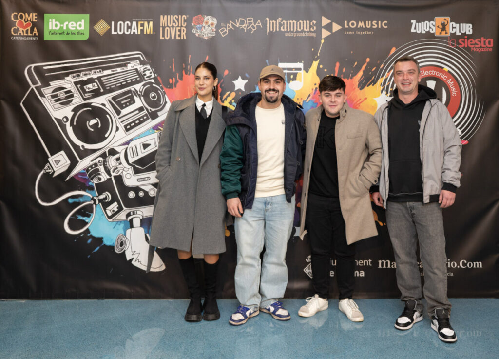 Cuatro personas posando en un evento de premios con un fondo colorido.