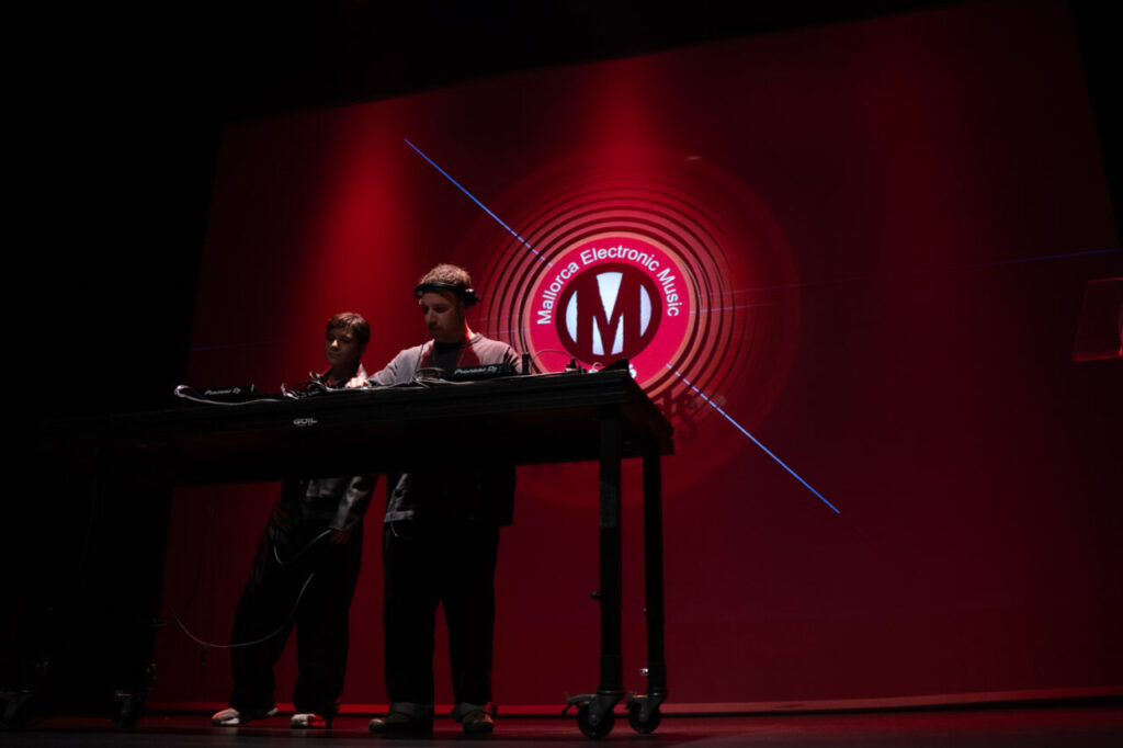Dos DJs actuando en un evento de música electrónica con fondo rojo.