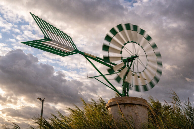 Molino de viento verde y blanco girando bajo un cielo nublado