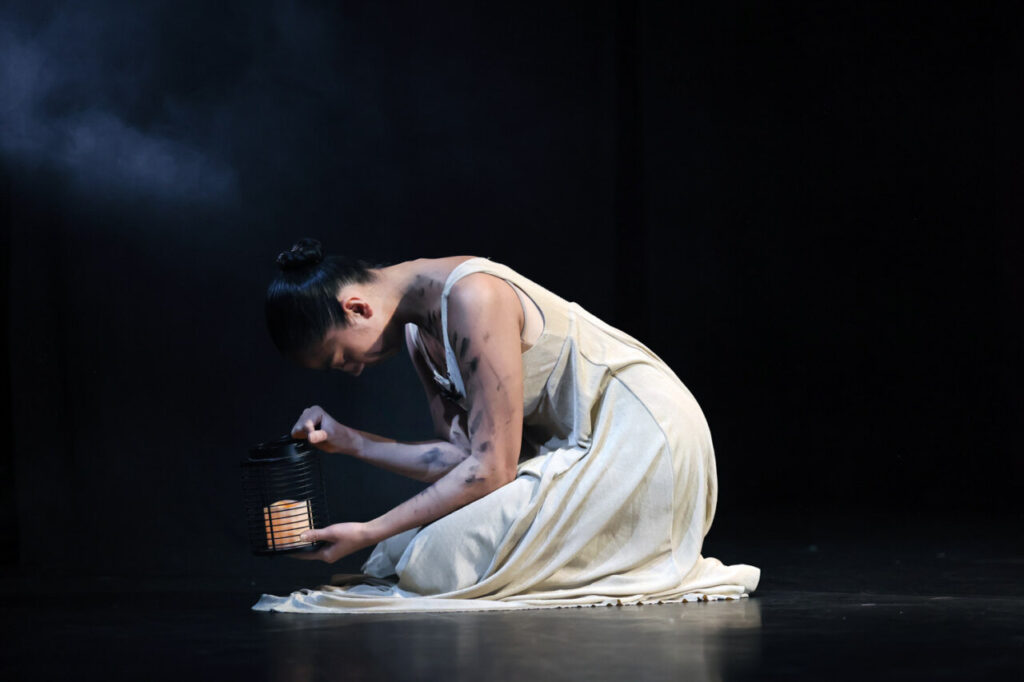 Bailarina interactuando con una lámpara en un escenario oscuro