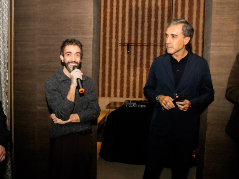 Dos hombres en un evento, uno habla con un micrófono.