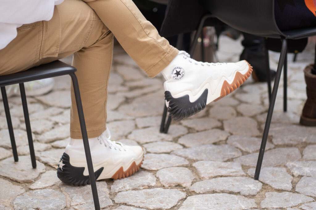 Persona sentada con pantalones beige y zapatillas Converse blancas