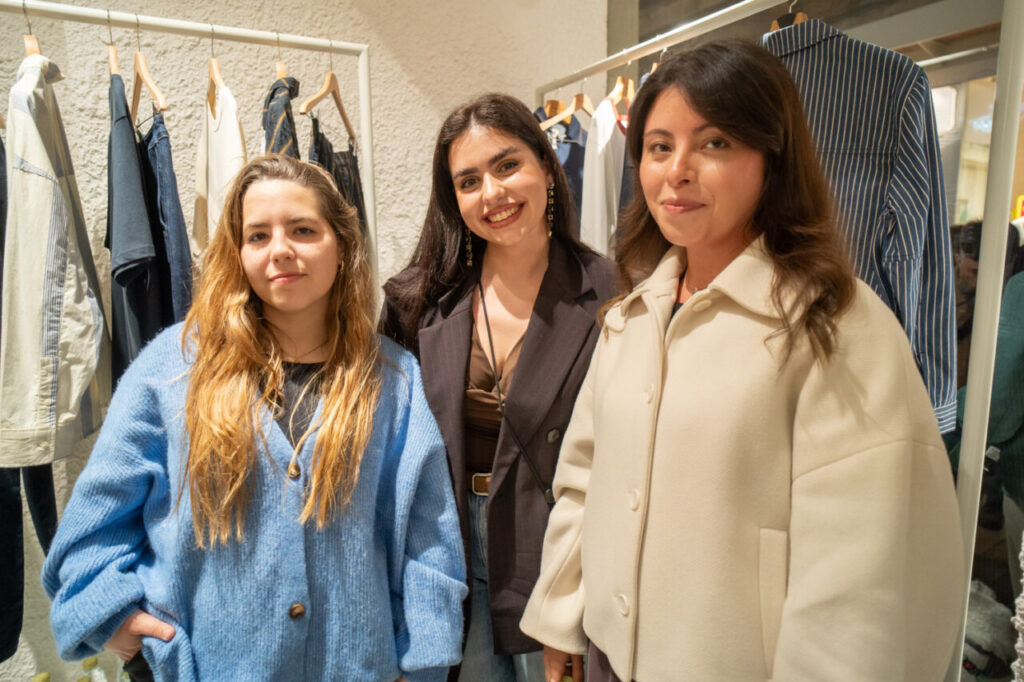 Tres mujeres posando en la tienda Thinking MU con ropa de fondo