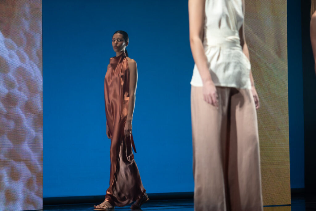 Modelo en pasarela con vestido de seda marrón en evento de moda