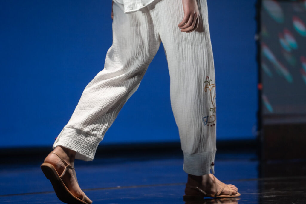 Modelo caminando en pasarela con pantalones blancos y sandalias