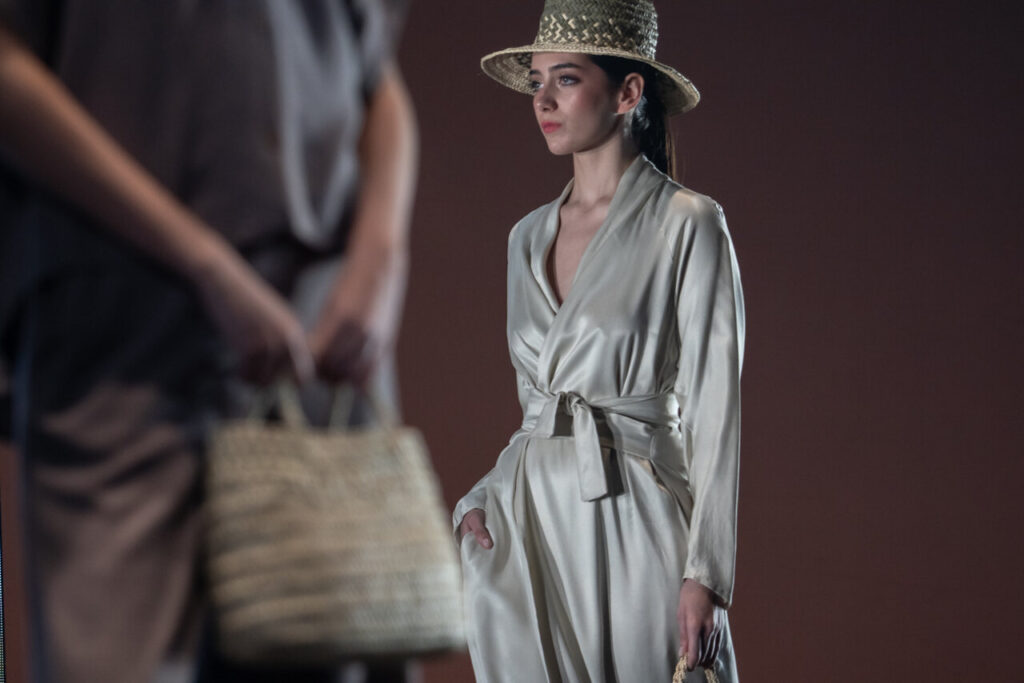 Modelo en pasarela con vestido de seda y sombrero de paja