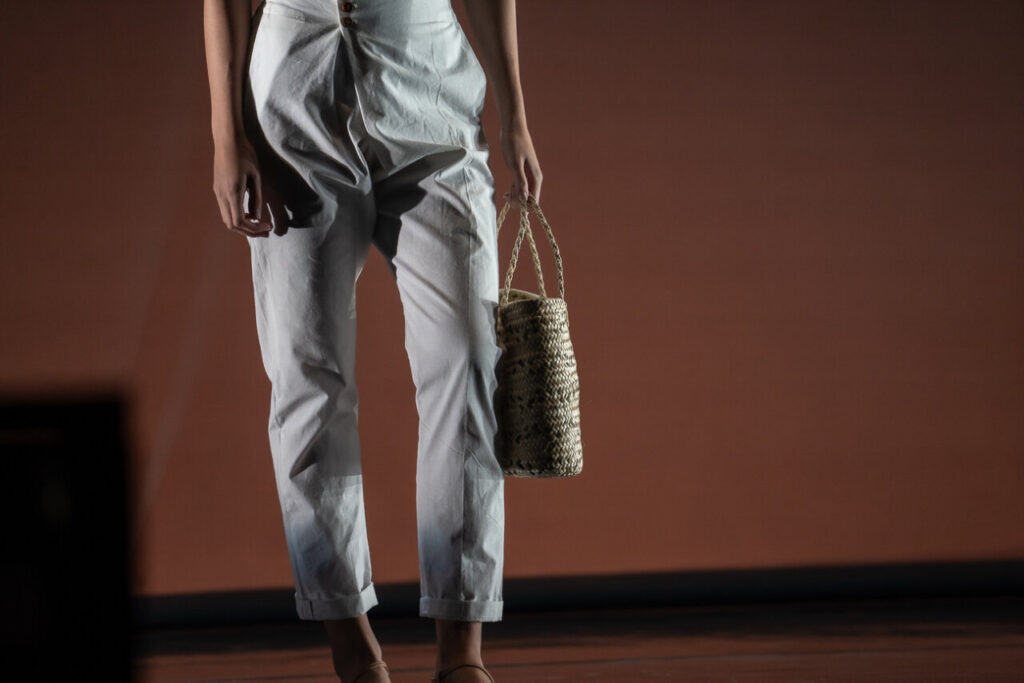 Modelo en pasarela mostrando ropa y bolso artesanal en evento de moda