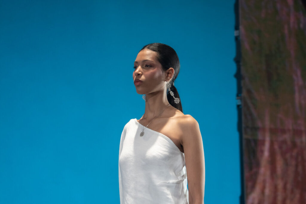 Modelo en pasarela con vestido blanco y pendientes brillantes