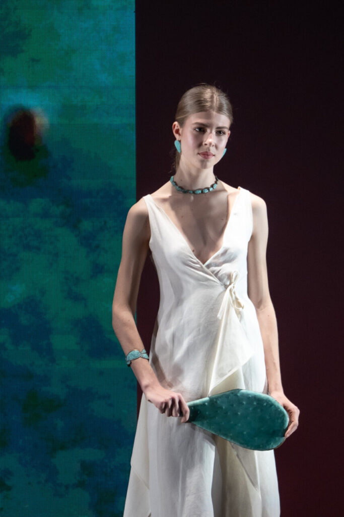 Modelo luciendo vestido blanco con accesorios artesanales en desfile de moda