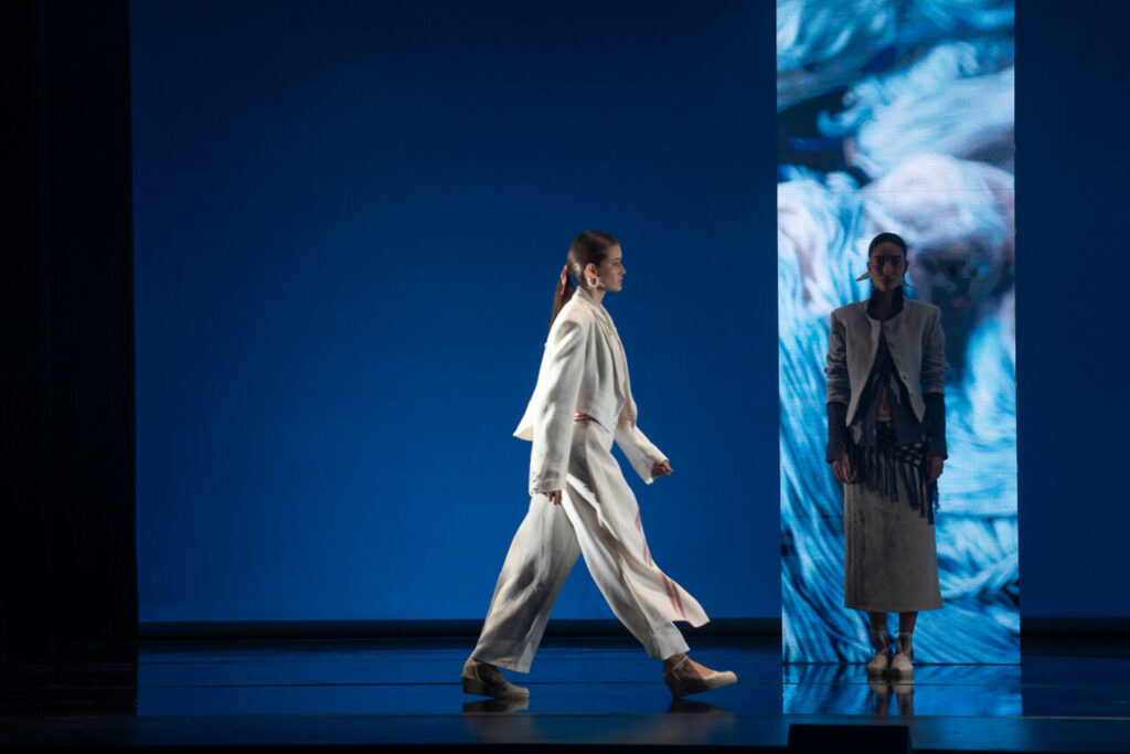 Modelo caminando en pasarela con fondo azul durante desfile de moda