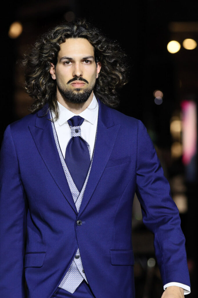 Modelo masculino con traje azul en pasarela de moda nupcial.