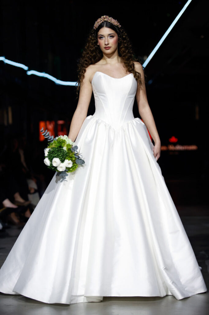 Modelo en pasarela con vestido de novia y ramo de flores en Motorworld