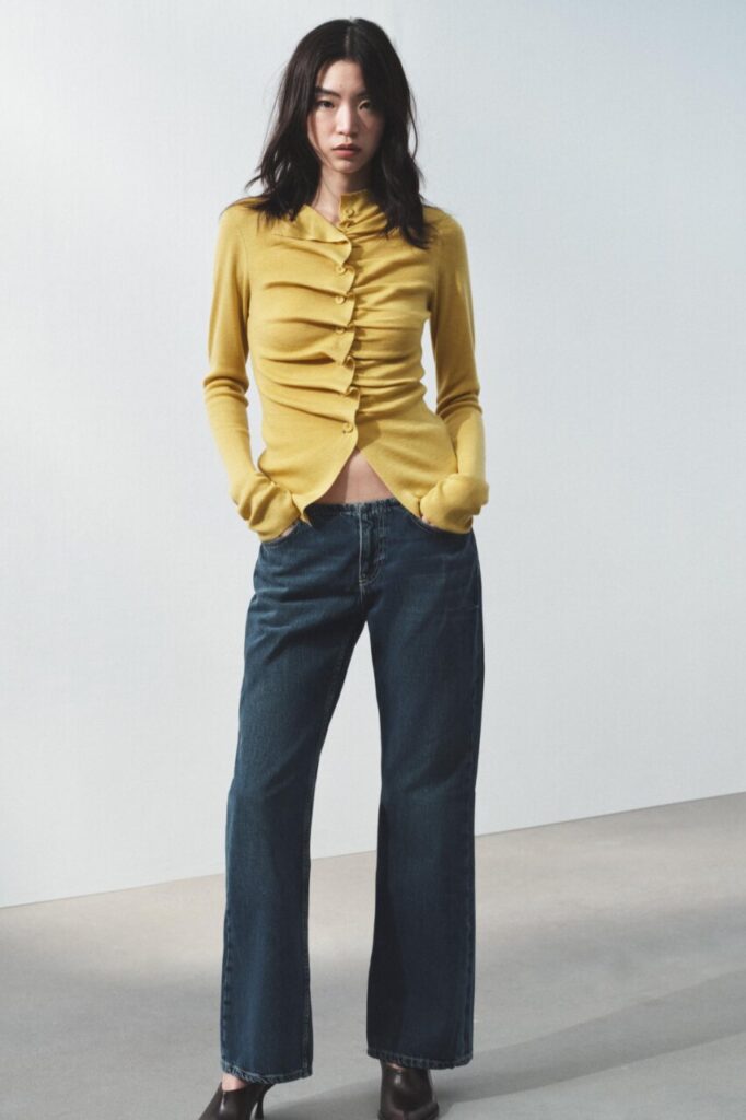 Modelo vistiendo chaqueta amarilla y jeans oscuros en fondo claro