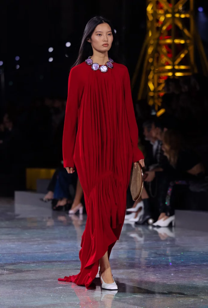 Modelo en pasarela con vestido rojo y collar llamativo en desfile de Chanel