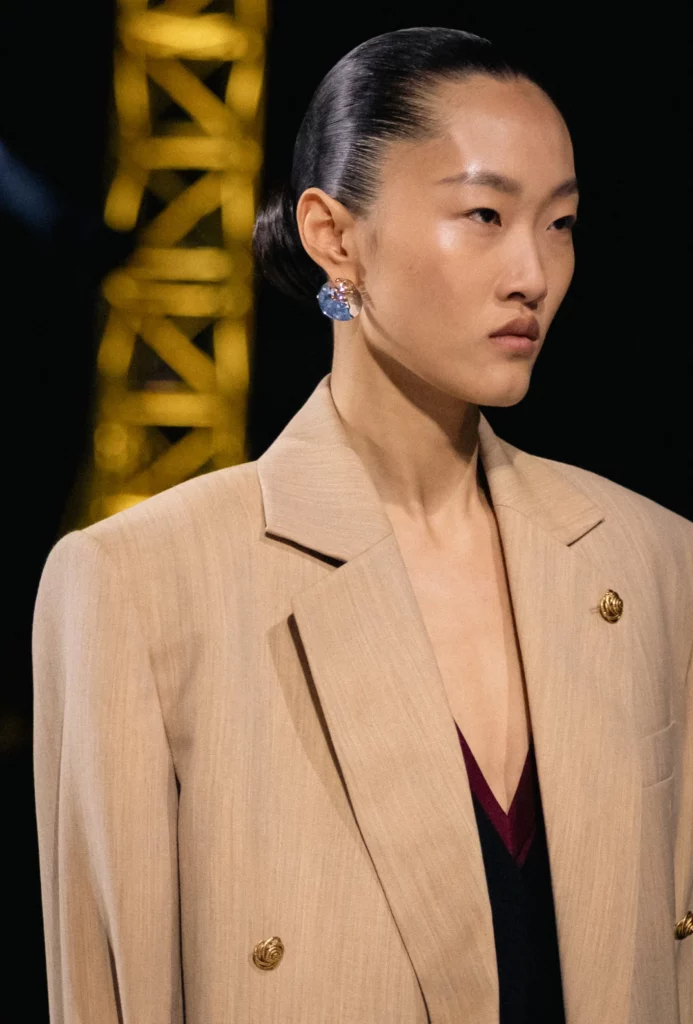 Modelo con chaqueta beige y pendientes en desfile de Chanel
