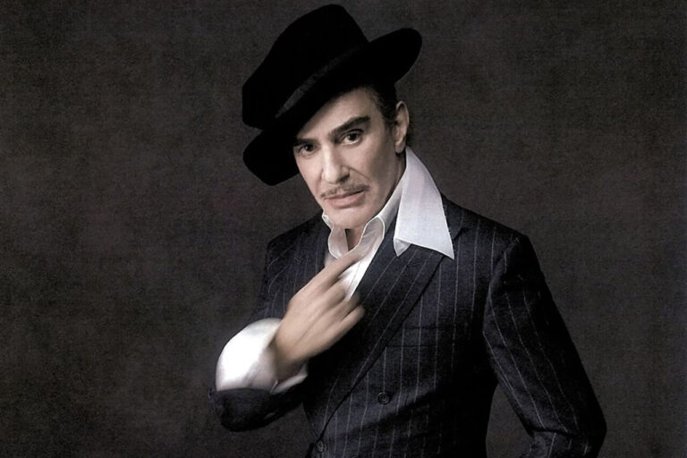 John Galliano posando con un elegante traje y sombrero