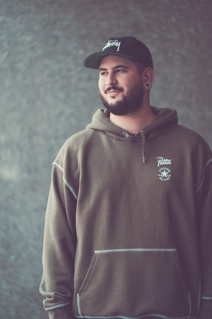 Hombre con barba y gorra de marca Stussy en un fondo gris