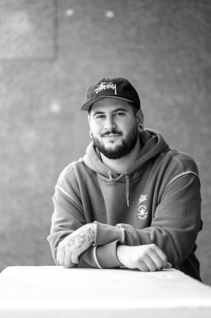 Hombre con barba y tatuajes sentado en una mesa con una sudadera gris