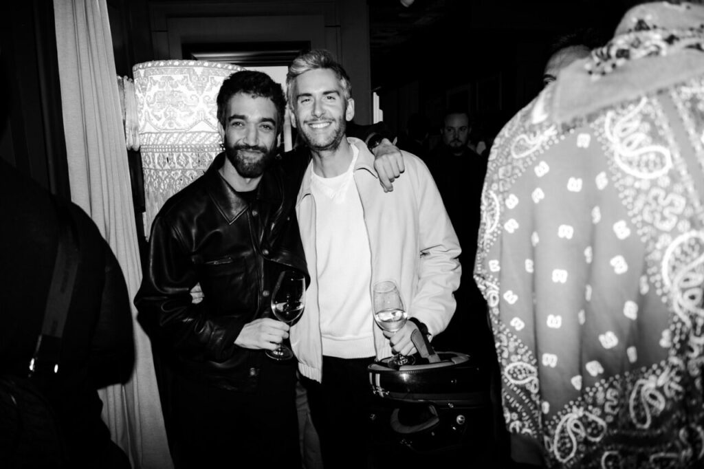 Dos hombres sonriendo en una fiesta con copas de vino.