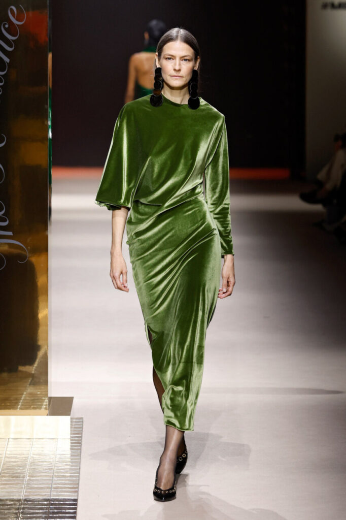 Modelo luciendo vestido verde de terciopelo en pasarela de moda.