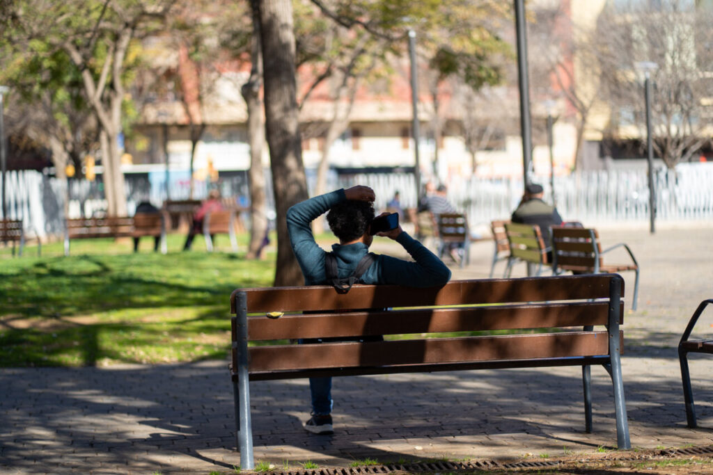Alergia en Baleares: lo que el calendario polínico de las islas revela sobre esta primavera 2 Persona sentada en un banco de parque usando su teléfono móvil.