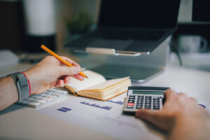Persona usando calculadora y escribiendo en un cuaderno sobre finanzas