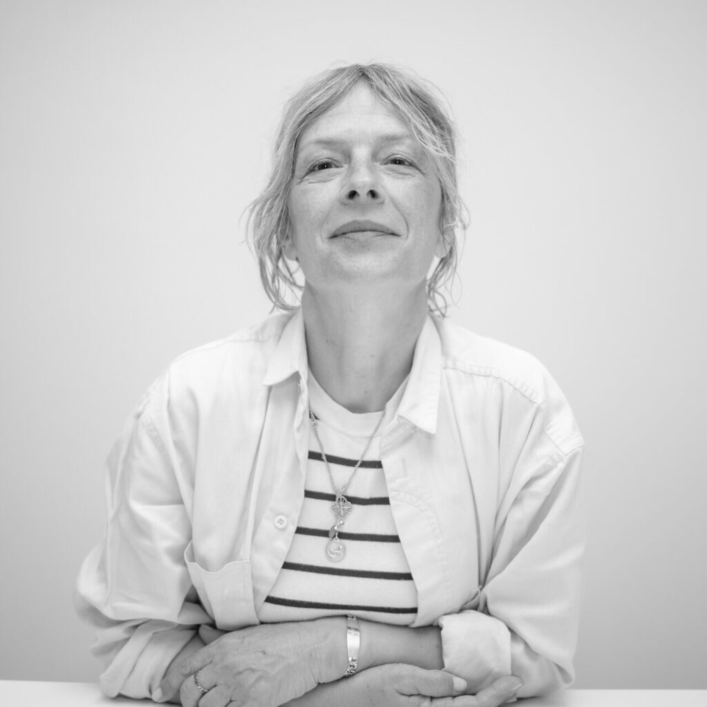 Mujer con cabello despeinado y blusa blanca sonriendo en un fondo claro