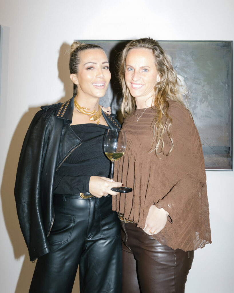 Dos mujeres posando en un evento de moda con copas de vino