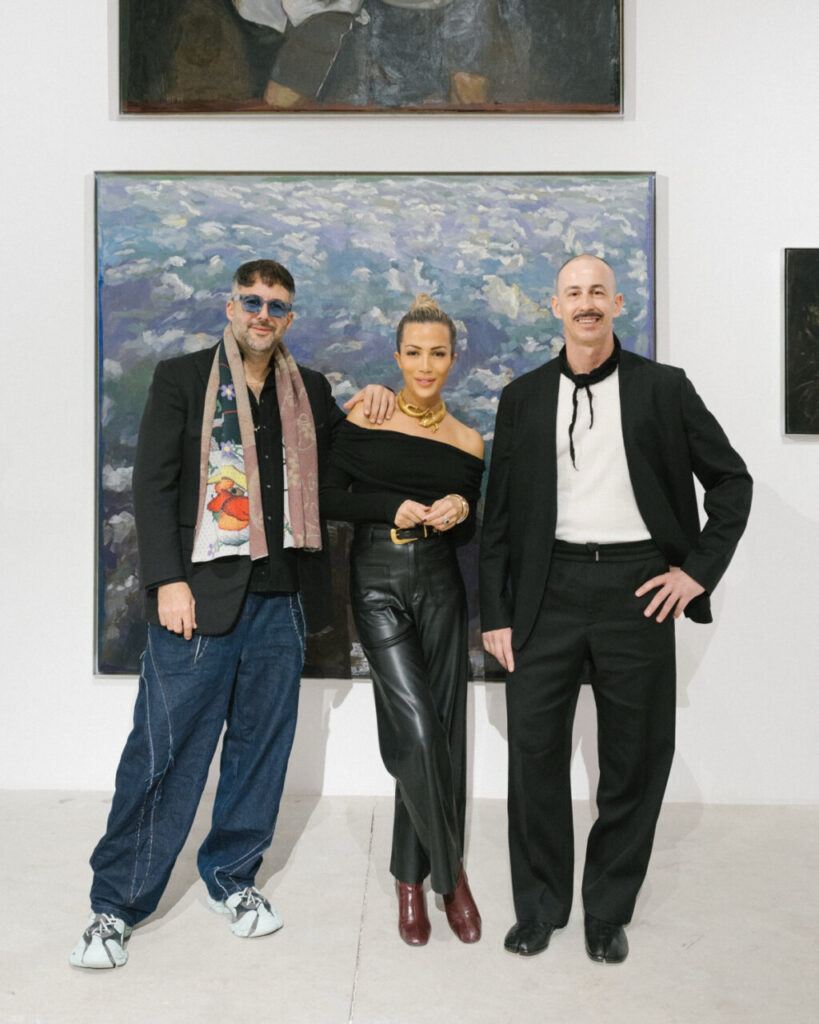 Tres personas posando en una galería de arte con pinturas de fondo