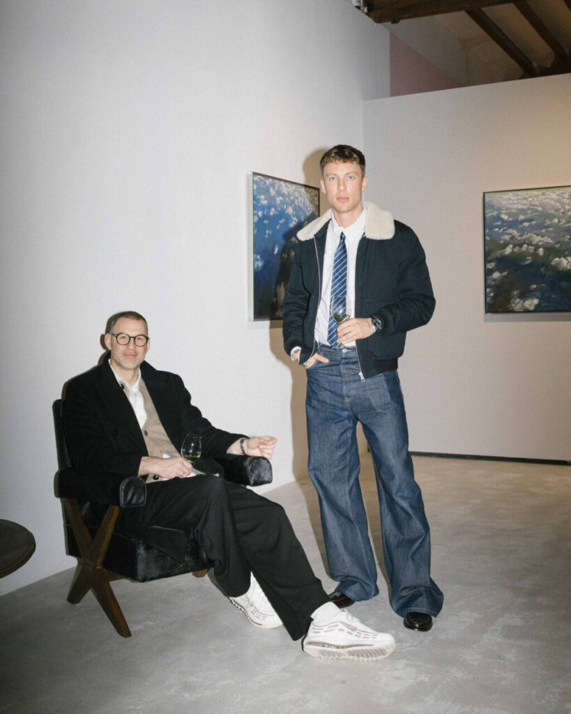 Dos hombres posando en una galería de arte con ropa de moda.