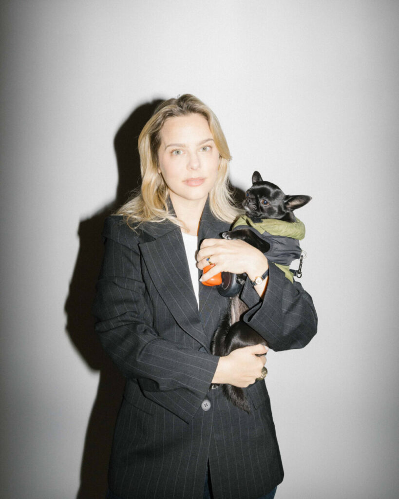 Mujer con chaqueta negra sosteniendo un perro en un entorno artístico