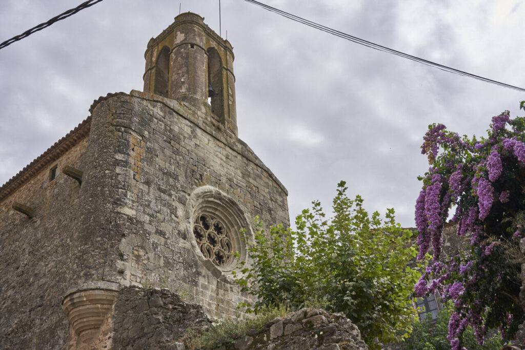 Peratallada: el pueblo medieval que detiene el tiempo en el Baix Empordà 8 Vista de una iglesia antigua con flores moradas alrededor