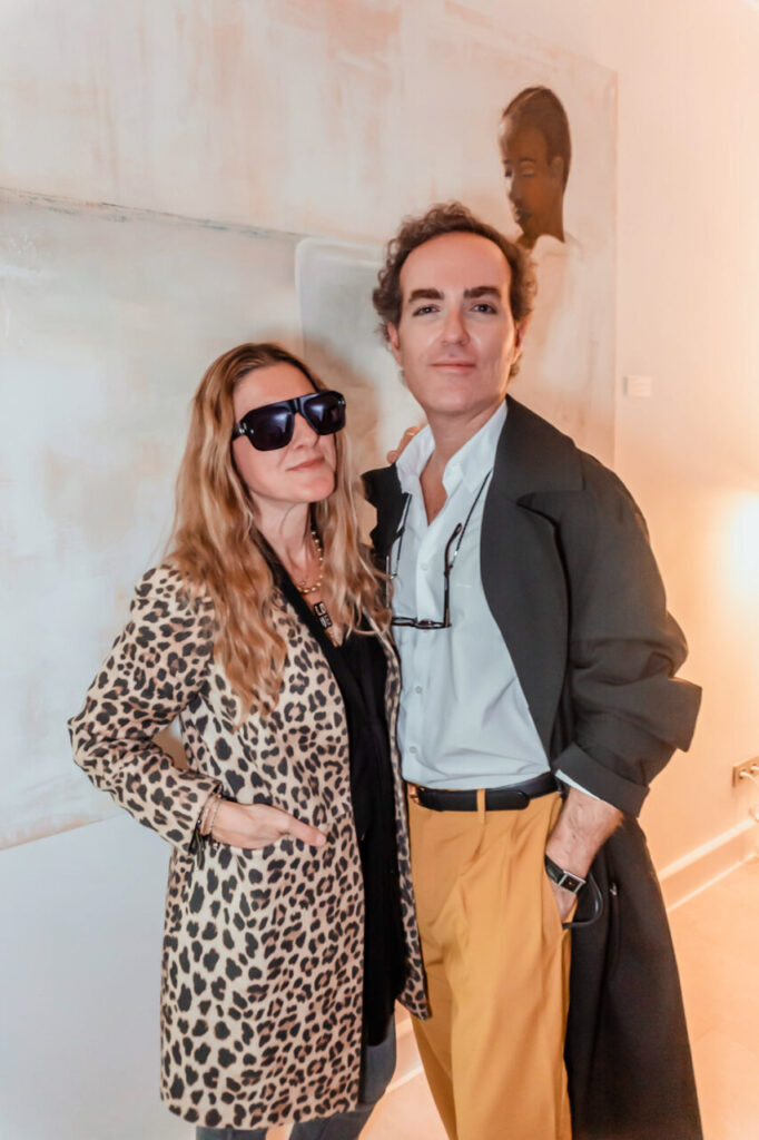 Dos personas posando en una galería de arte con una pintura de fondo.