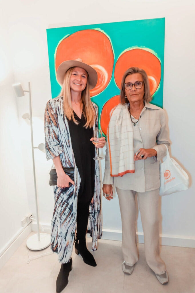 Dos mujeres posando en La Bibi Gallery frente a una pintura colorida