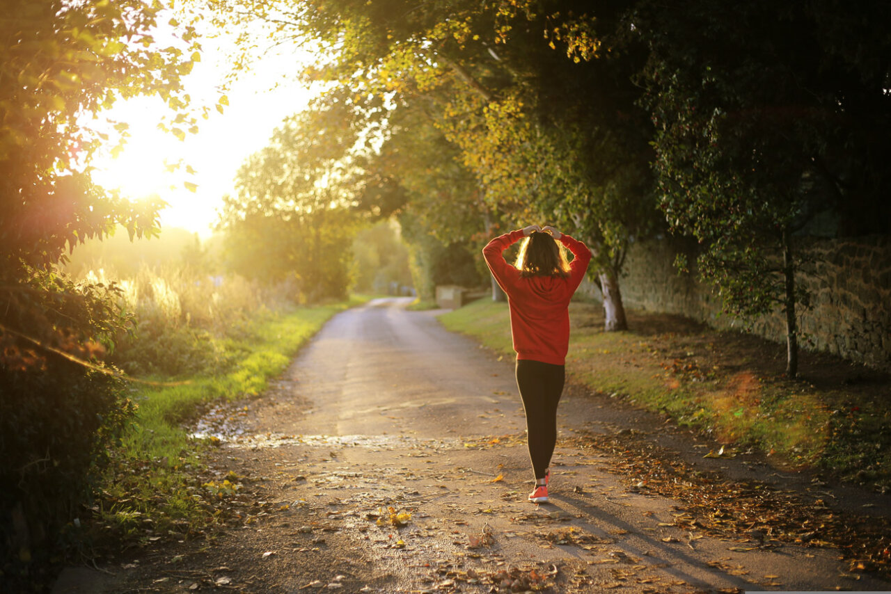 Mujer caminando por un sendero al atardecer rodeada de naturaleza