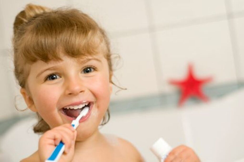 La importancia de las revisiones dentales para nuestra salud bucal 1 Niña sonriendo mientras se cepilla los dientes en el baño