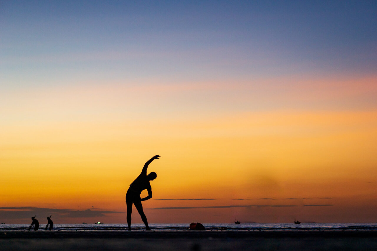 Persona estirándose en la playa durante el amanecer