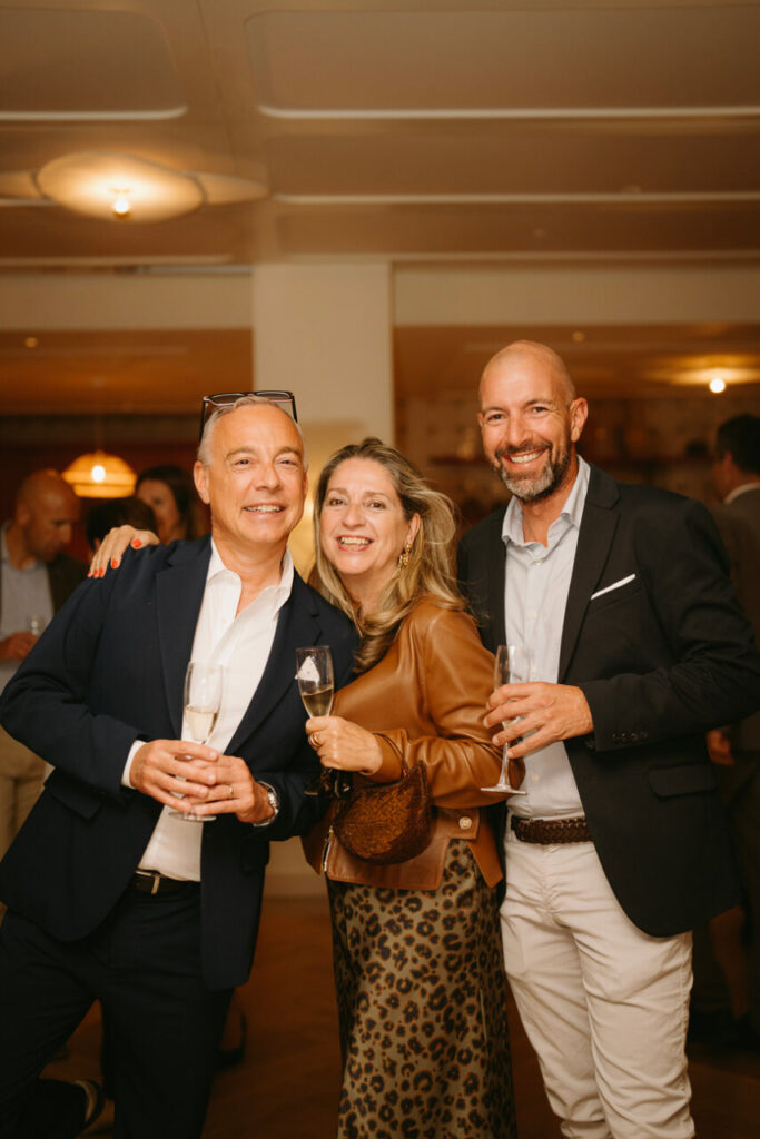 Tres personas sonrientes sosteniendo copas en un evento social