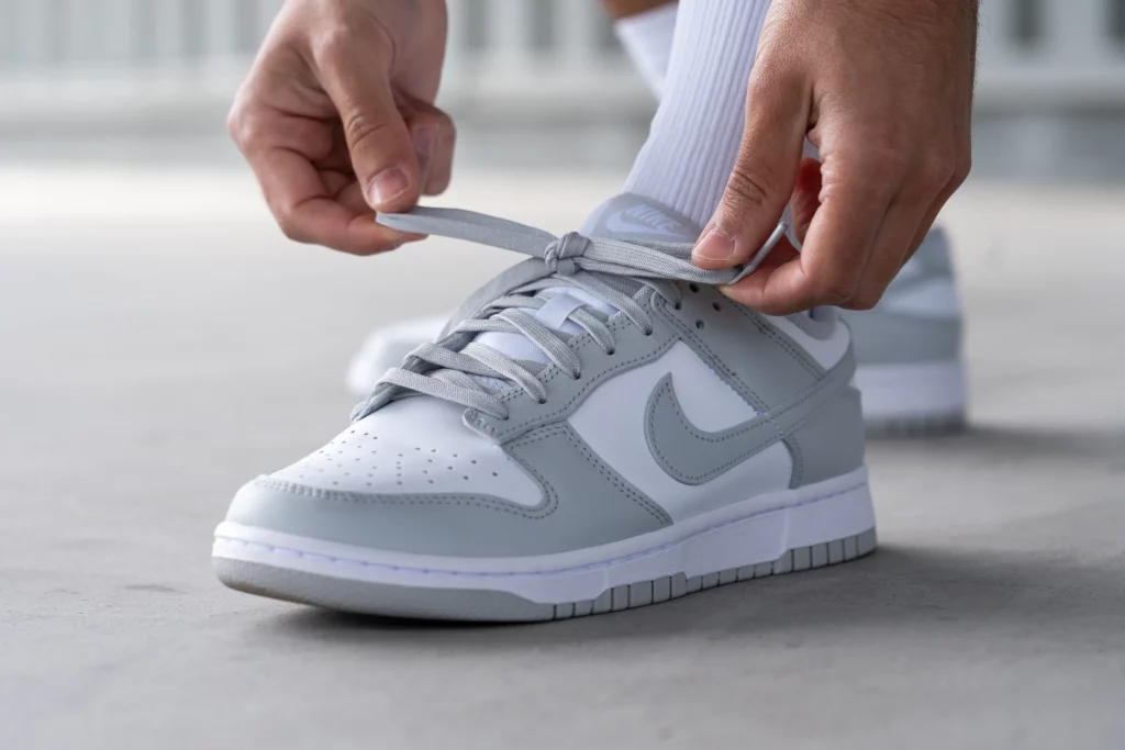 Persona ajustando los cordones de unas zapatillas Nike Dunk Low grises