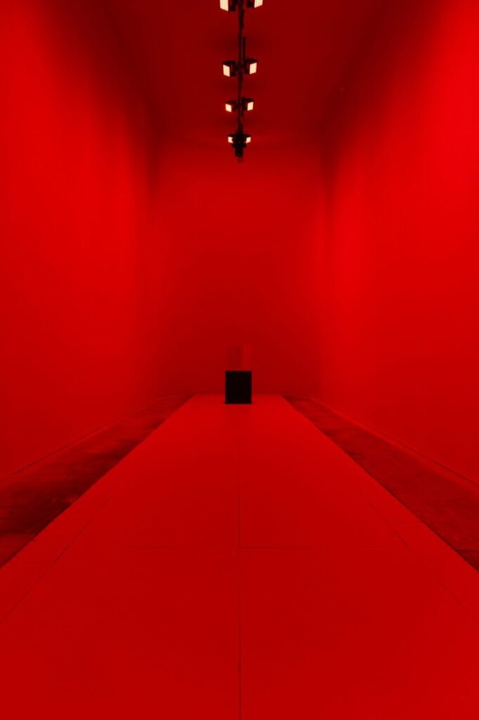 Interior de una galería con paredes rojas y un pedestal negro