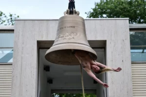 Performance artística con una campana y un artista colgando